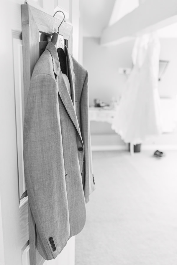 fine art wedding photography hereford ross on wye - groom's suit hanging from a door and bride's dress hanging from a bed on the morning of their wedding - image by hayley morris photography 