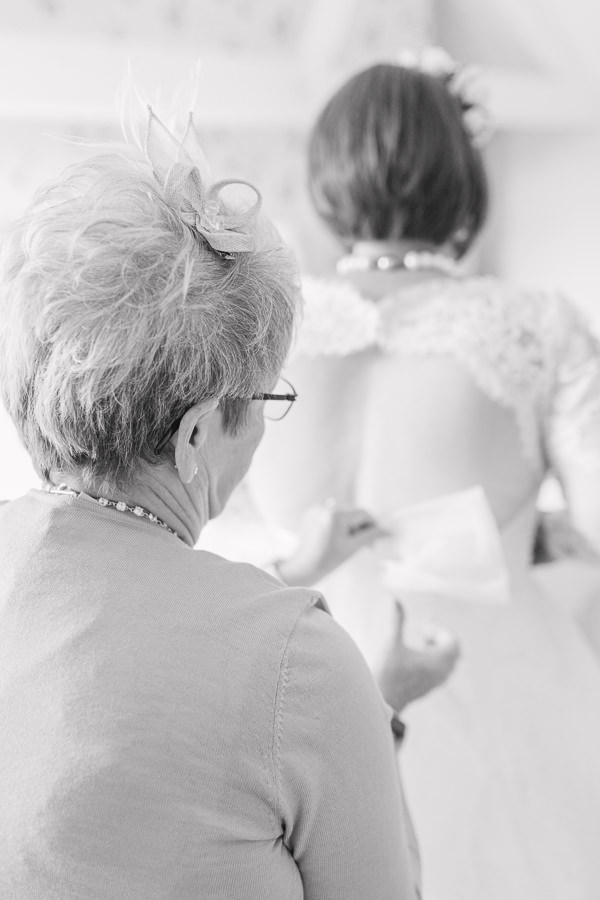 ross on wye fine art wedding photography hereford herefordshire - image shows a mum helping her daughter to get dressed on the morning of her wedding by doing her dress up - image by hayley morris photography