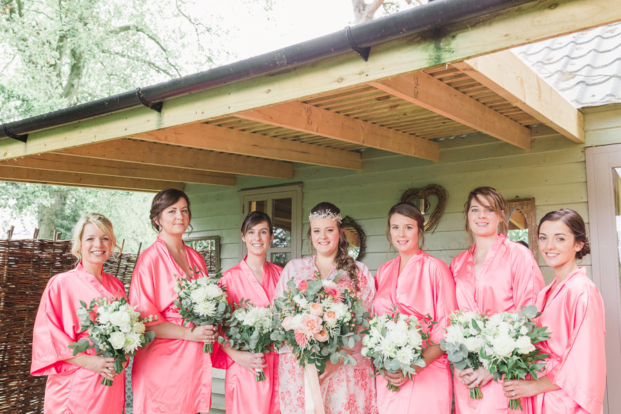 image of bridesmaids and brides stood outside the hen house at  lemore manor hereford herefordshire, the ladies are all wearing dressing gowns and holding their bouquets - image by hayley morris photography 