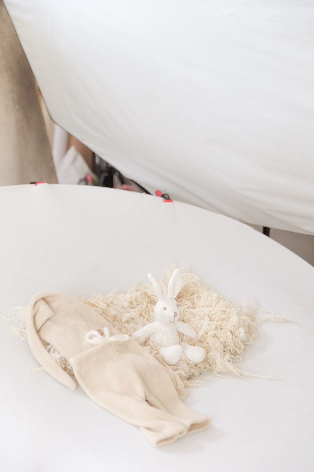Newborn posing bag prepped with neutral wool layer, bunny and romper. In the background there is a studio light in my studio at hayley morris phtography near malvern