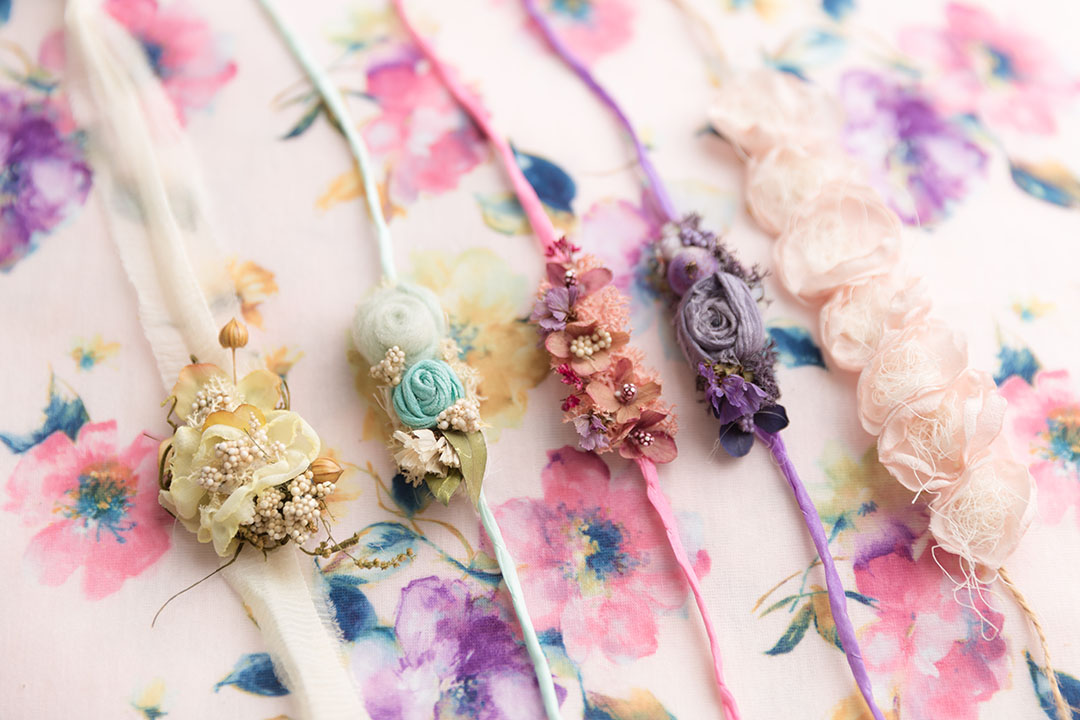 Floral pastel backdrop fabric with 5 floral headbands in coordinating colours of purple, yellow, aqua and pinks lay on the fabric