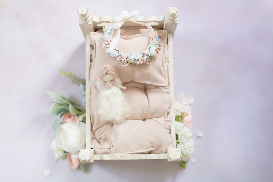 pale pink backdrop on the floor with vintage newborn posing bed, dusky pink mattress and fairy, handmade baby flower crown and flowers to the side of the bed. The set is ready for a baby phootography session
