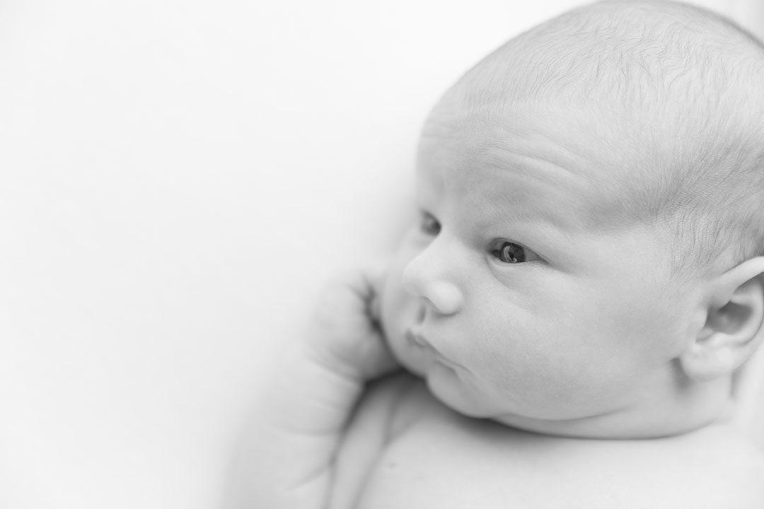 black and white photo of a newborn baby lay with their eyes open, close up of their face. They are lay on a posing bag for newborn studio photography 