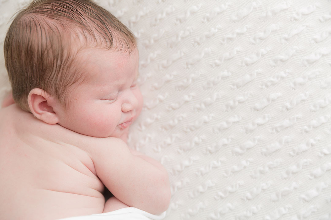 baby lay on their side, posed on a posing bag for newborn baby photos on a white textured fabric  