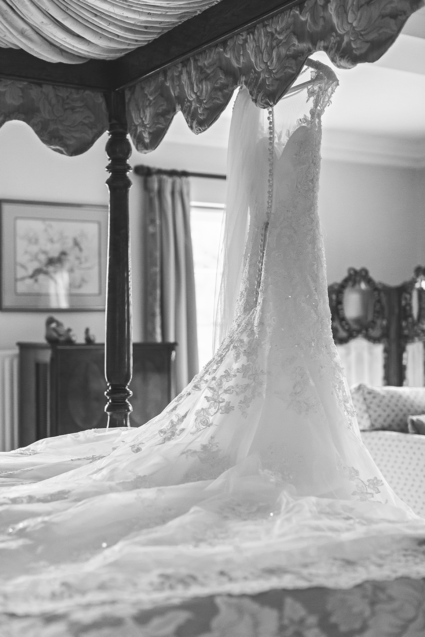 Black and white photo of a bride's dress hanging from a four poster bed in the manor house of birtsmorton course