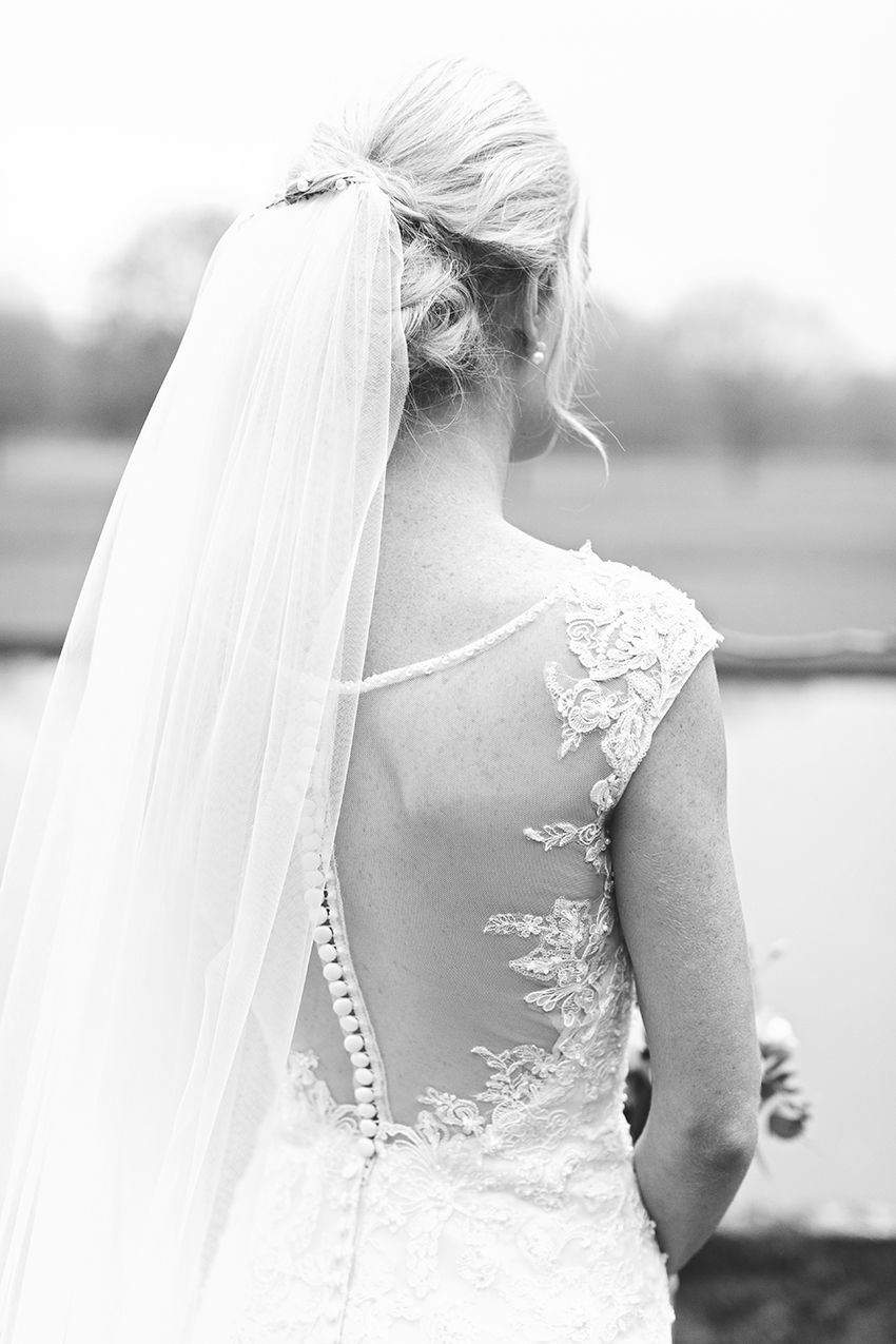 Bride wearing a veil captured from behind stood with a moat at birtsmorton court behind her