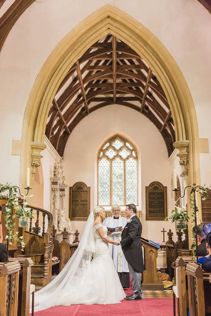 Birtsmorton Court church - couple stood in front of a vicar exchanging wedding vows. Photo taken from the end of the aisle
