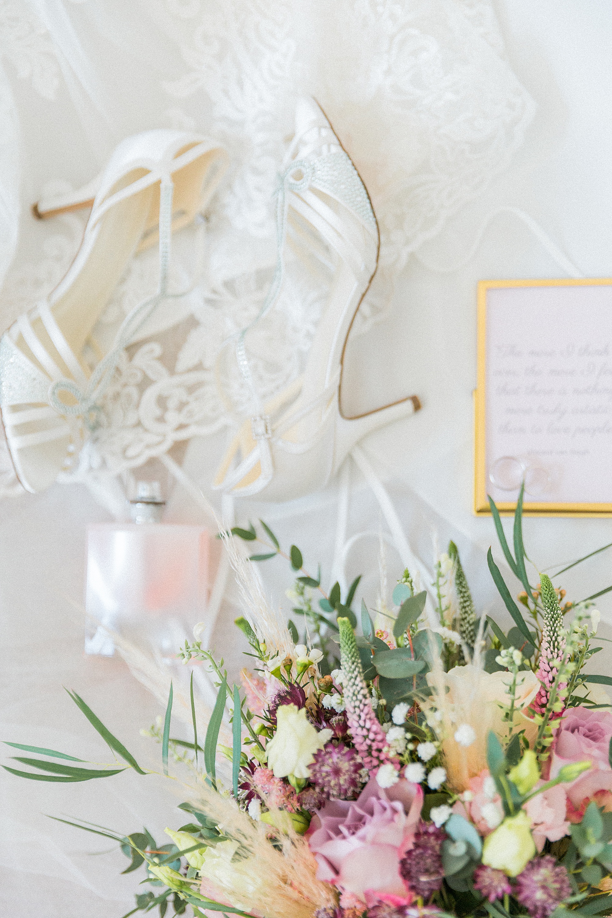 image shows the bride's wedding details like her shoes, flowers, jewellery etc posed and placed in an arrangement on the morning of her wedding against her dress and veil