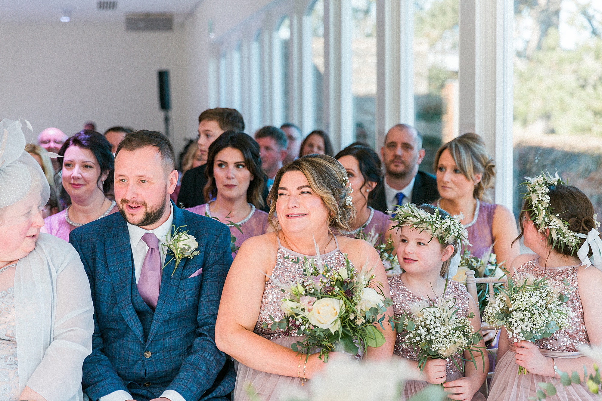 photo of bridesmaids and wedding guests looking towards the couple and smiling during the wedding ceremony