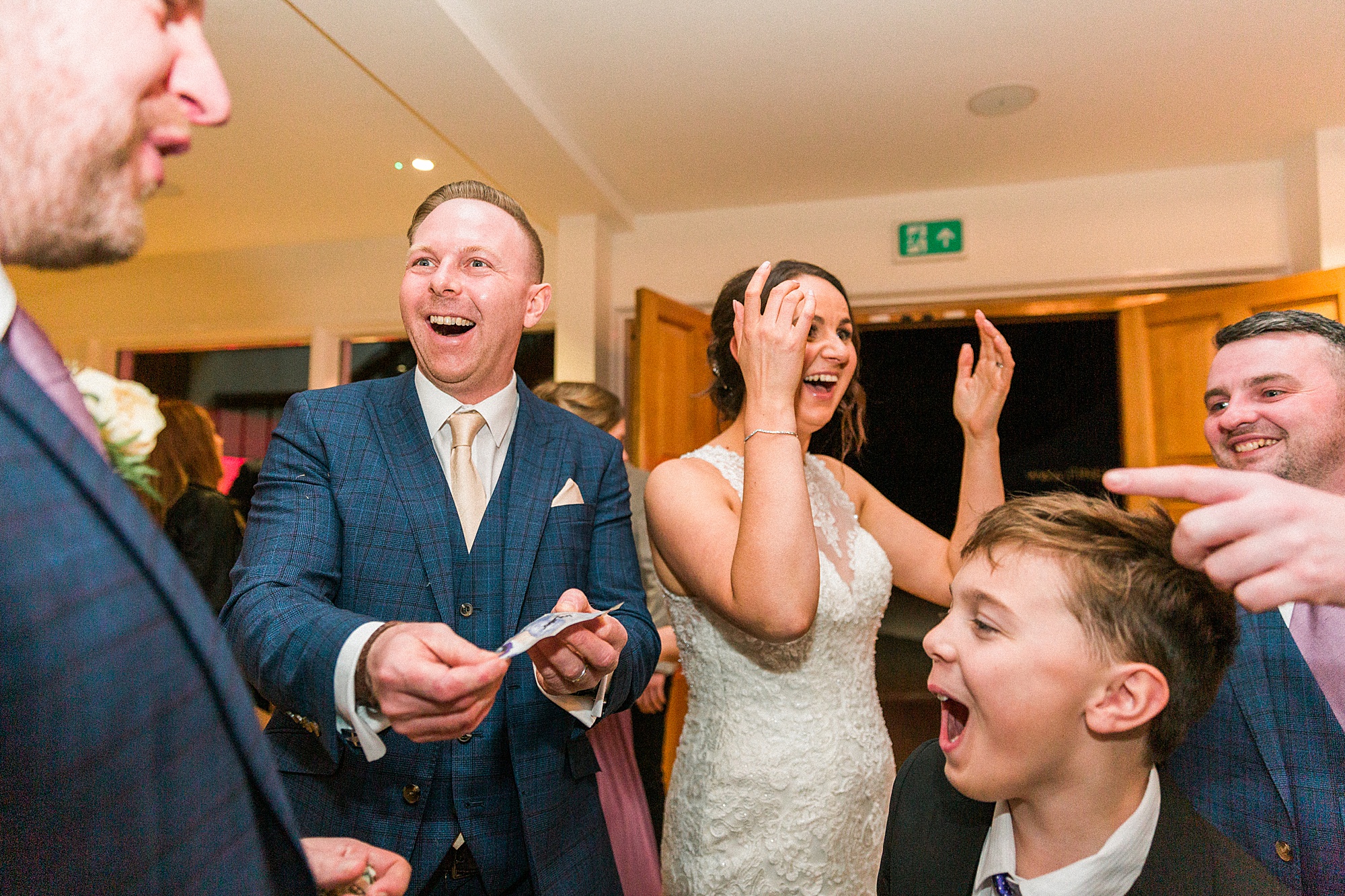 photo of a bride and groom surround with their guests. Photo captures their reaction to a magician's trick at arley house west midlands