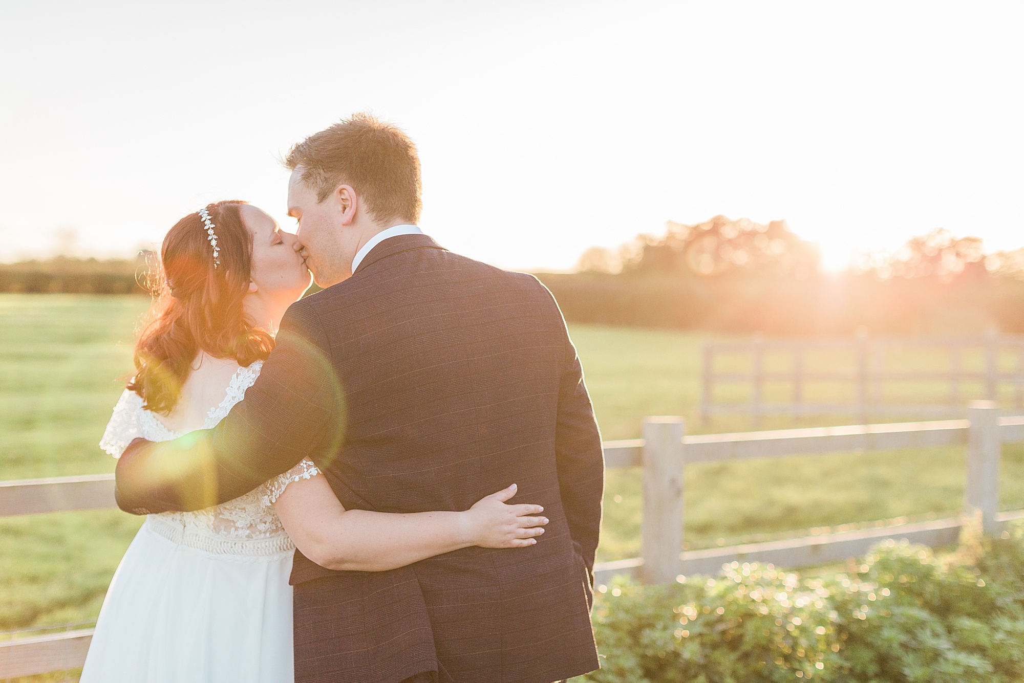 bride and groom stood with their backs to the camera embracing and kissing in the sunset at cider mill barns
