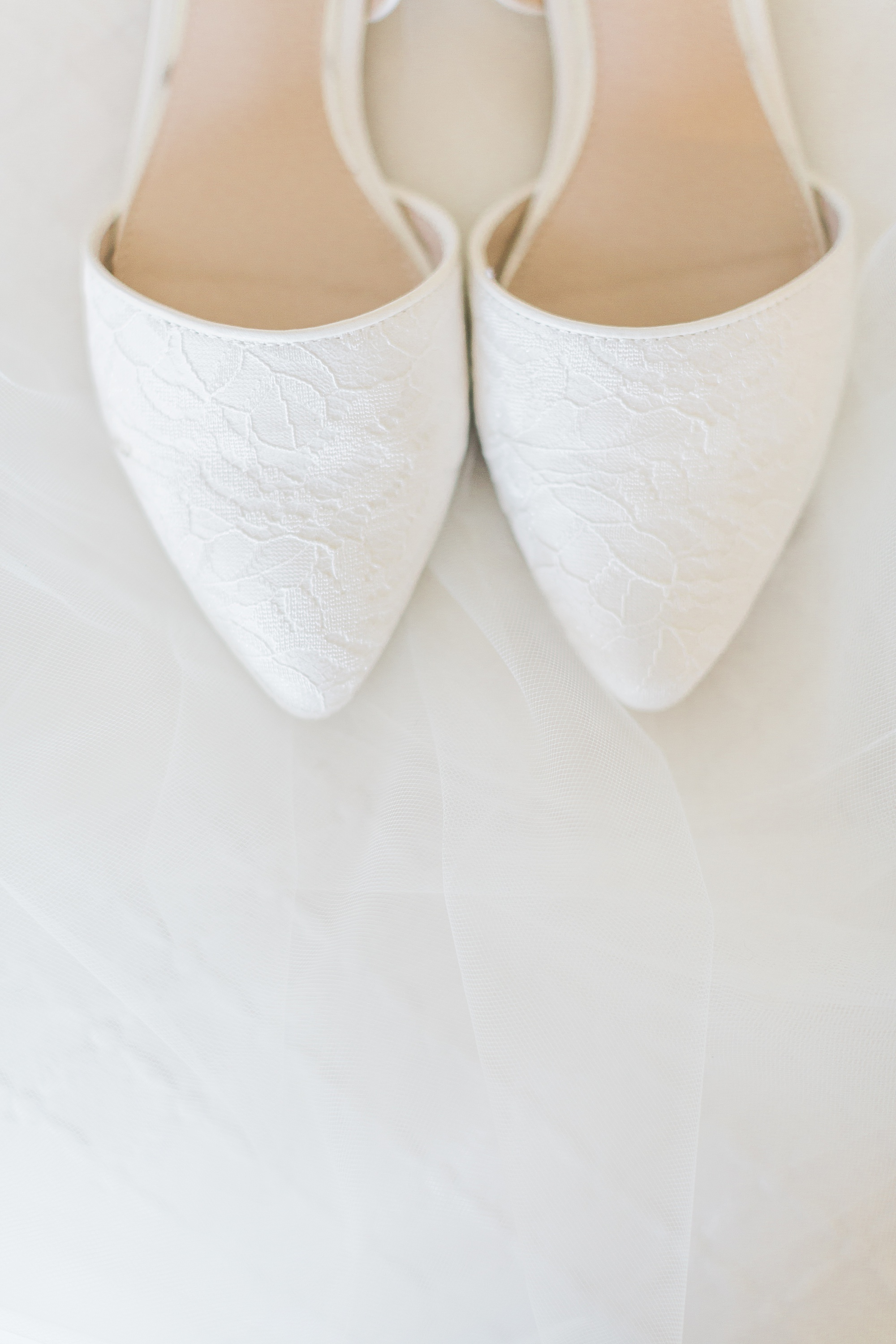 the front/tips/toes of white bridal shoes photographed against a white veil