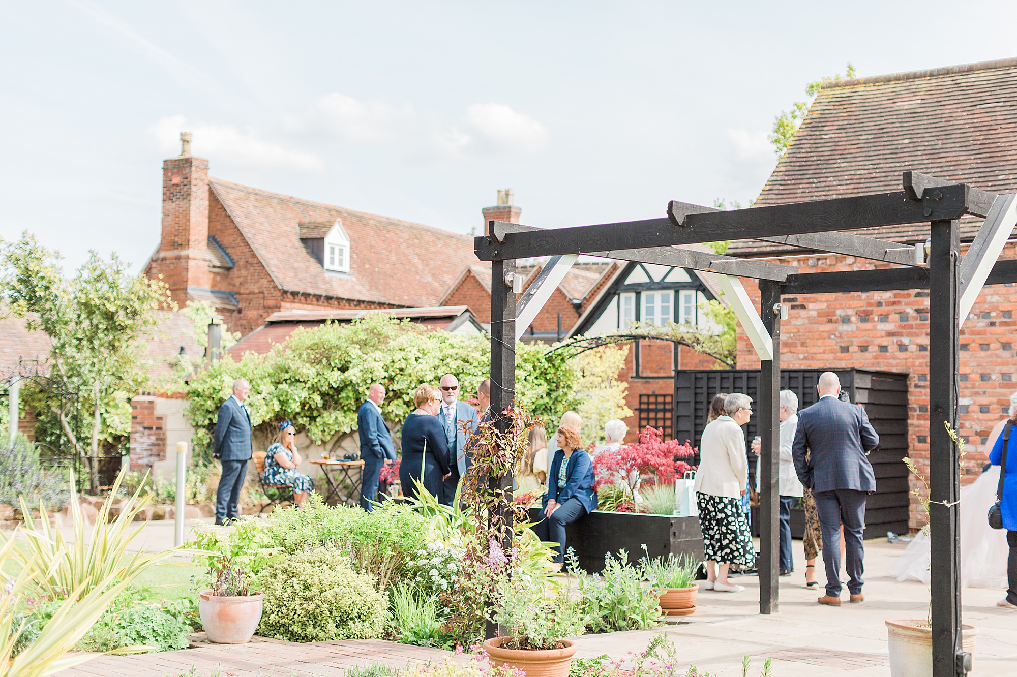 photo of a wedding reception at curradine barns. Guests are at the front gardens with the barns behind them enjoying drinks outside at a spring wedding