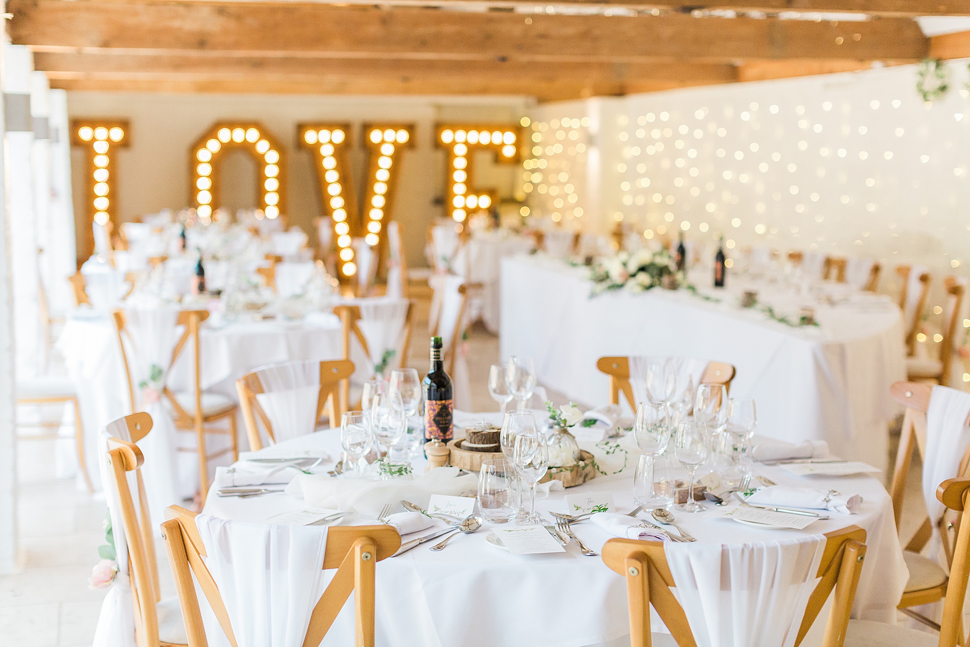 photo of a wedding reception at curradine barns ready for guests, beautiful tables laid ready with light love letters in the background 