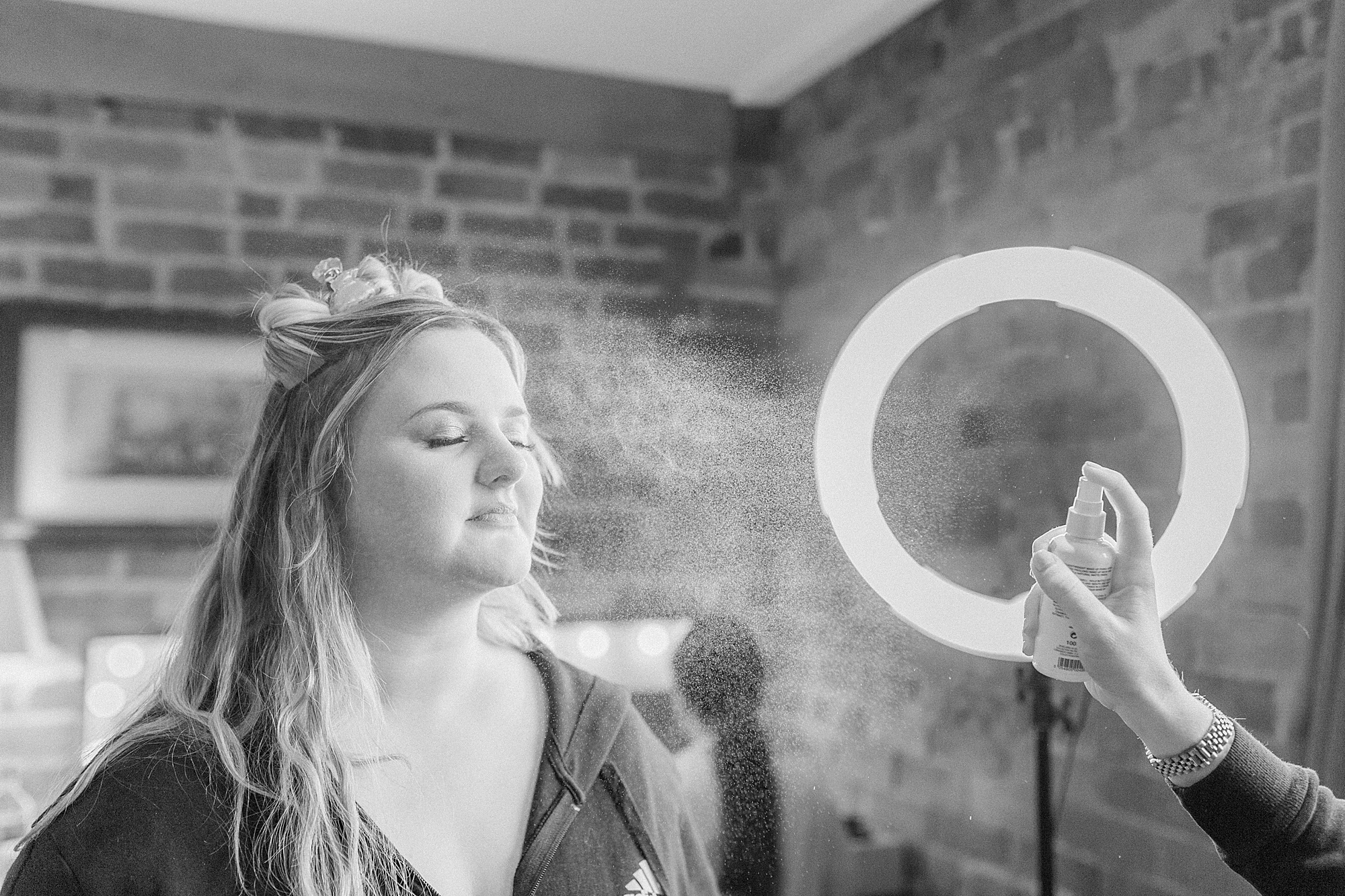 photo of a bride having setting spray sprayed over her face after having her makeup done ahead of her wedding day 