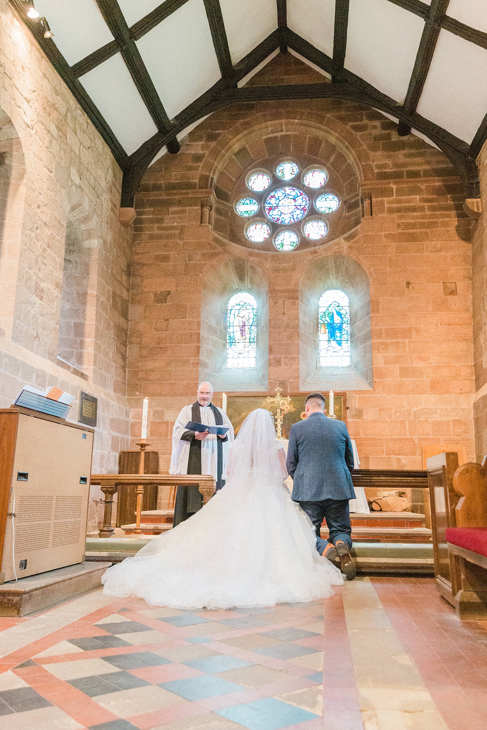 photo of a bride and groom kneeling during their wedding ceremony at the church in shrawley next to curradine barns