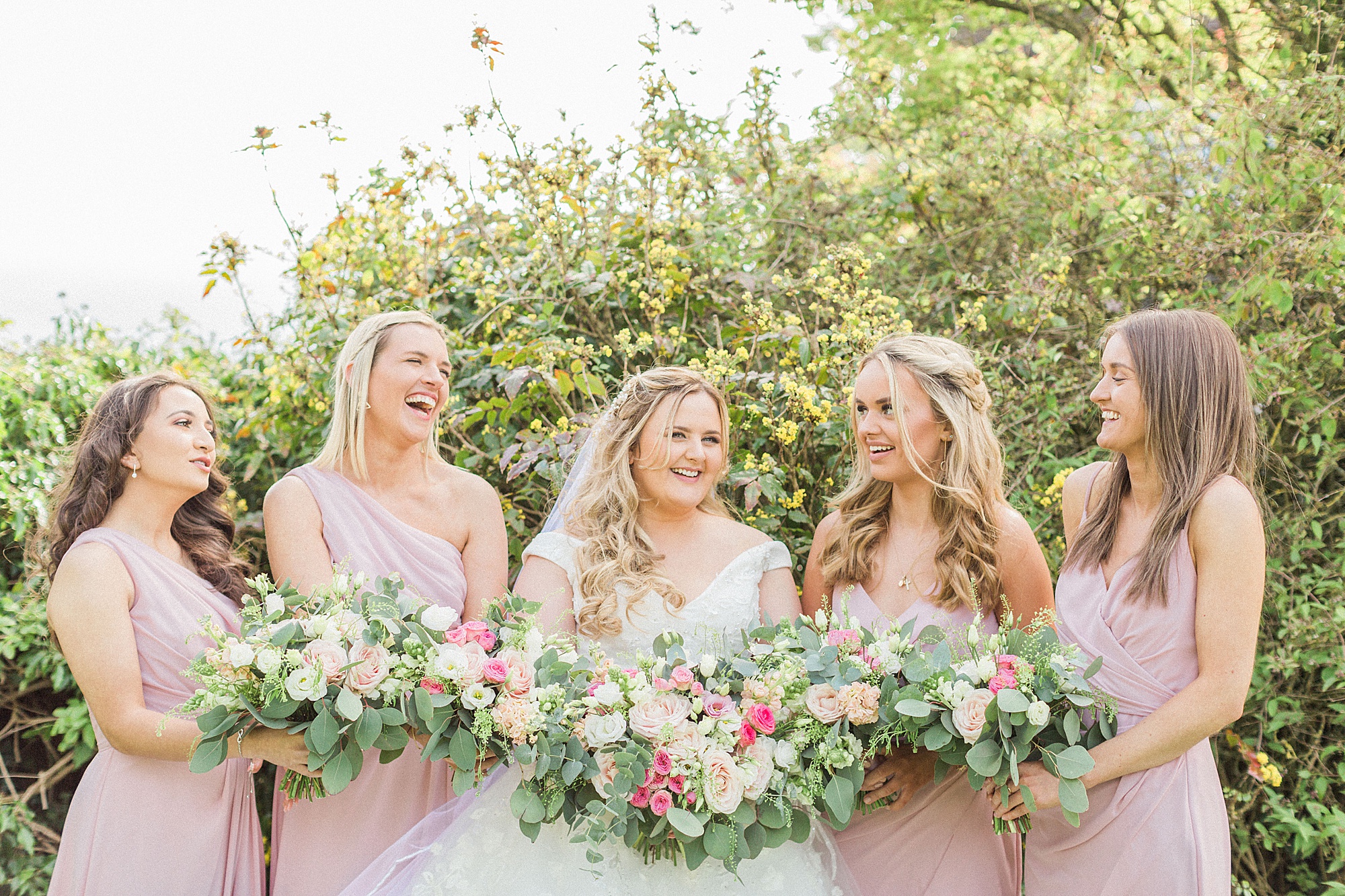 photo of a bride and her bridesmaids posed together smiling and laughing each holding their bouquets
