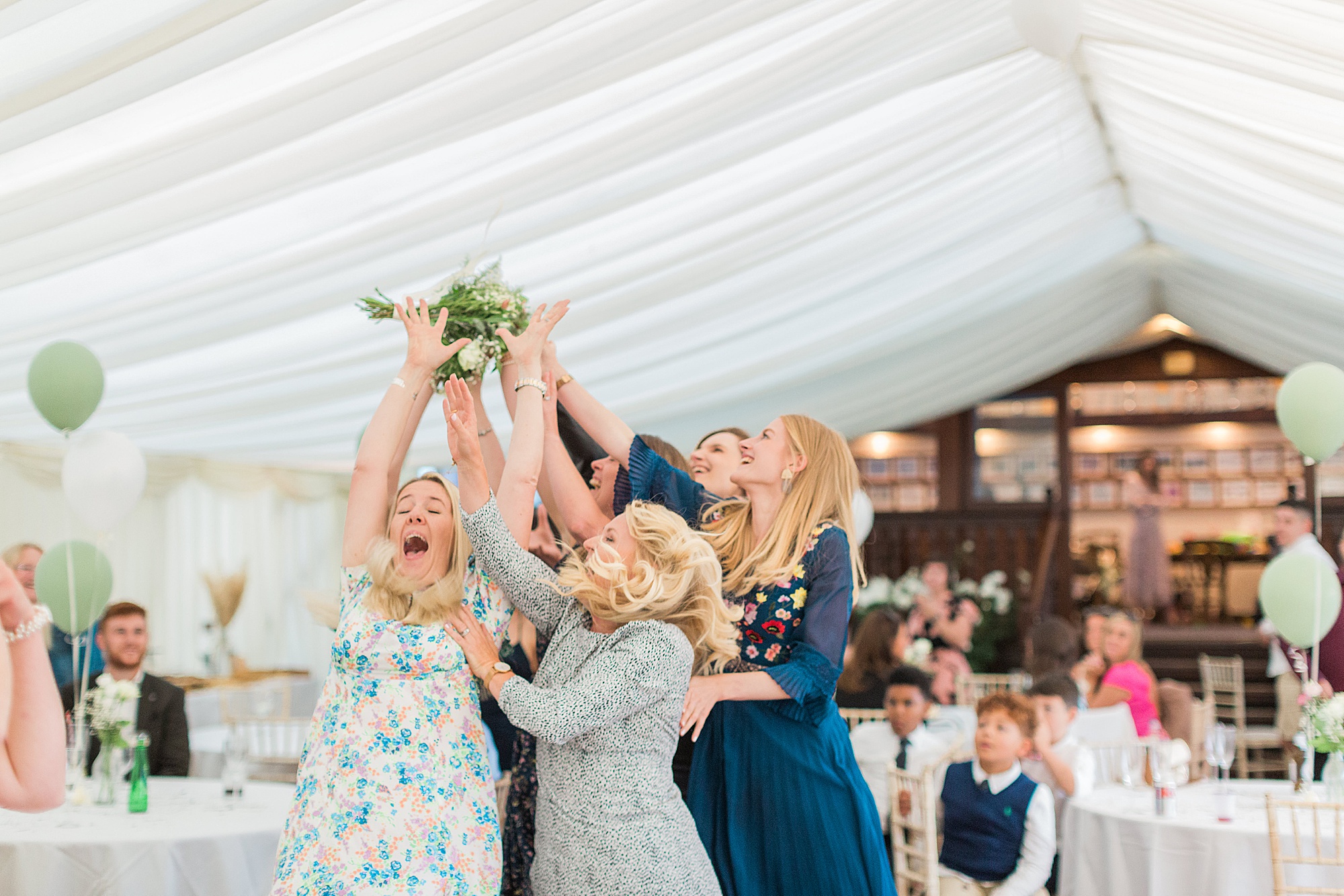 photo shows a group of female guests at a wedding stood on a dance floor about the catch the bouquet that the bride has just thrown