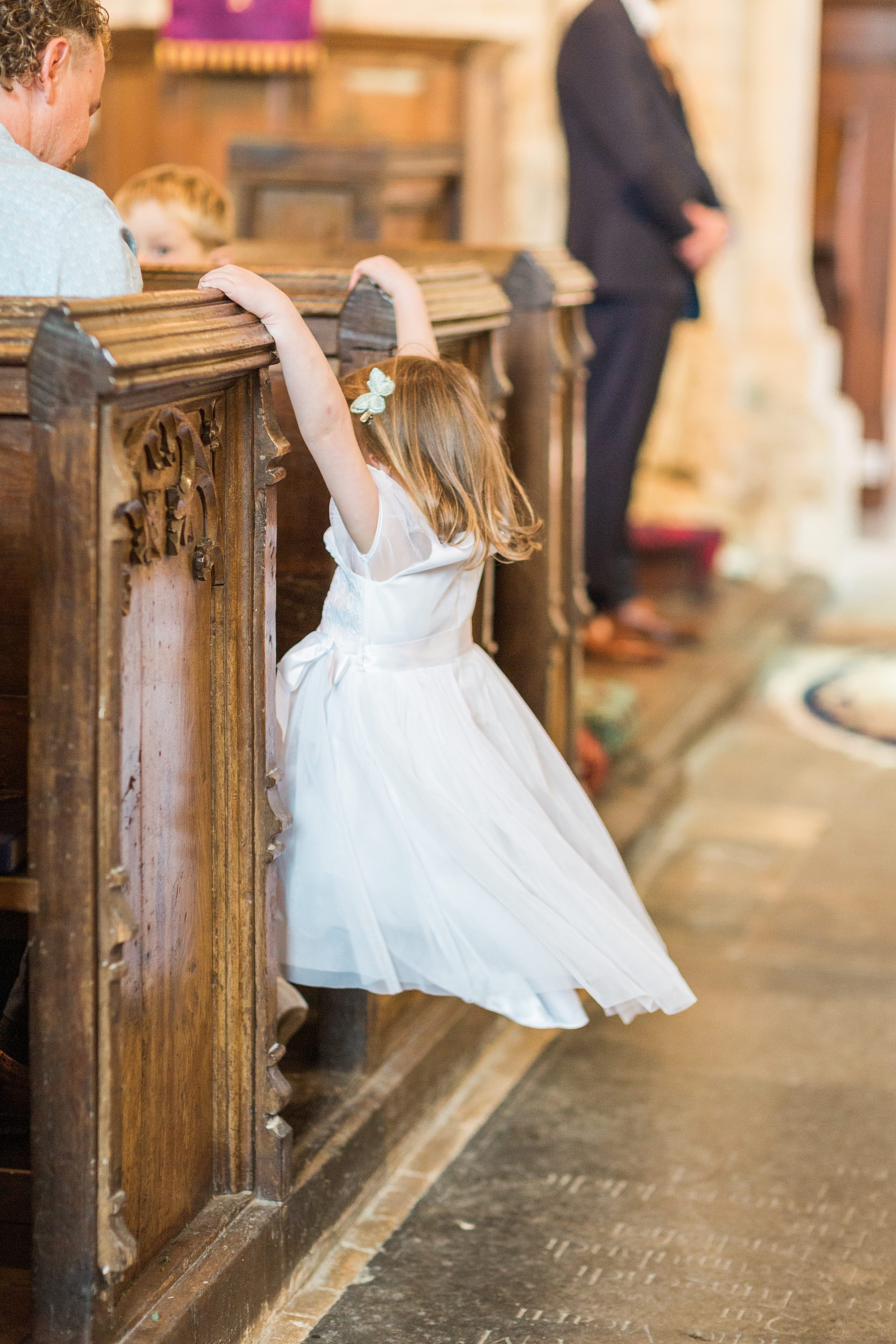 photo fo a flower girl swinging from the pews in a church at a wedding in the cotswolds near Dumbleton 