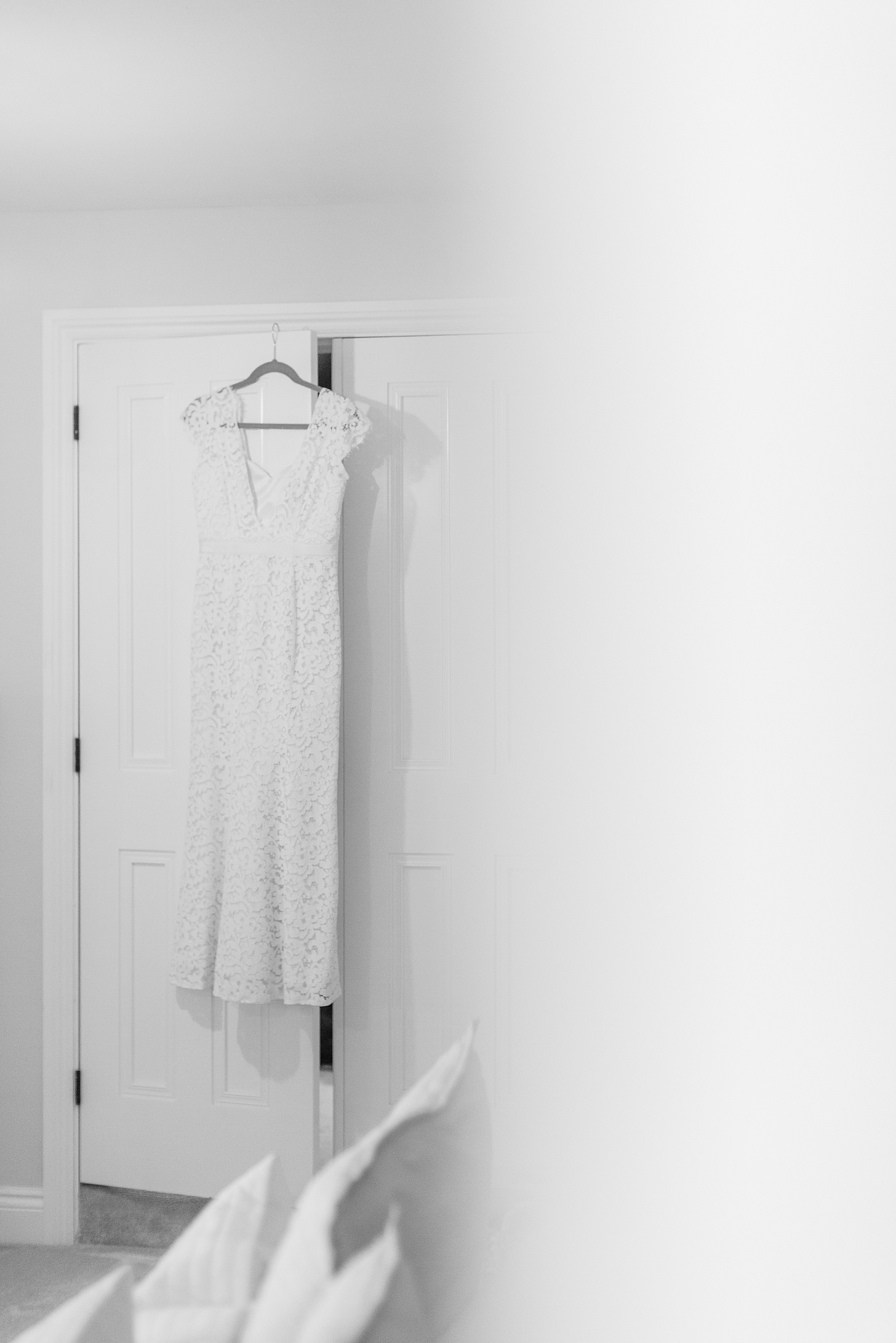 black and white photo of a lace bridal gown photographed through a doorway hanging from a wardrobe door