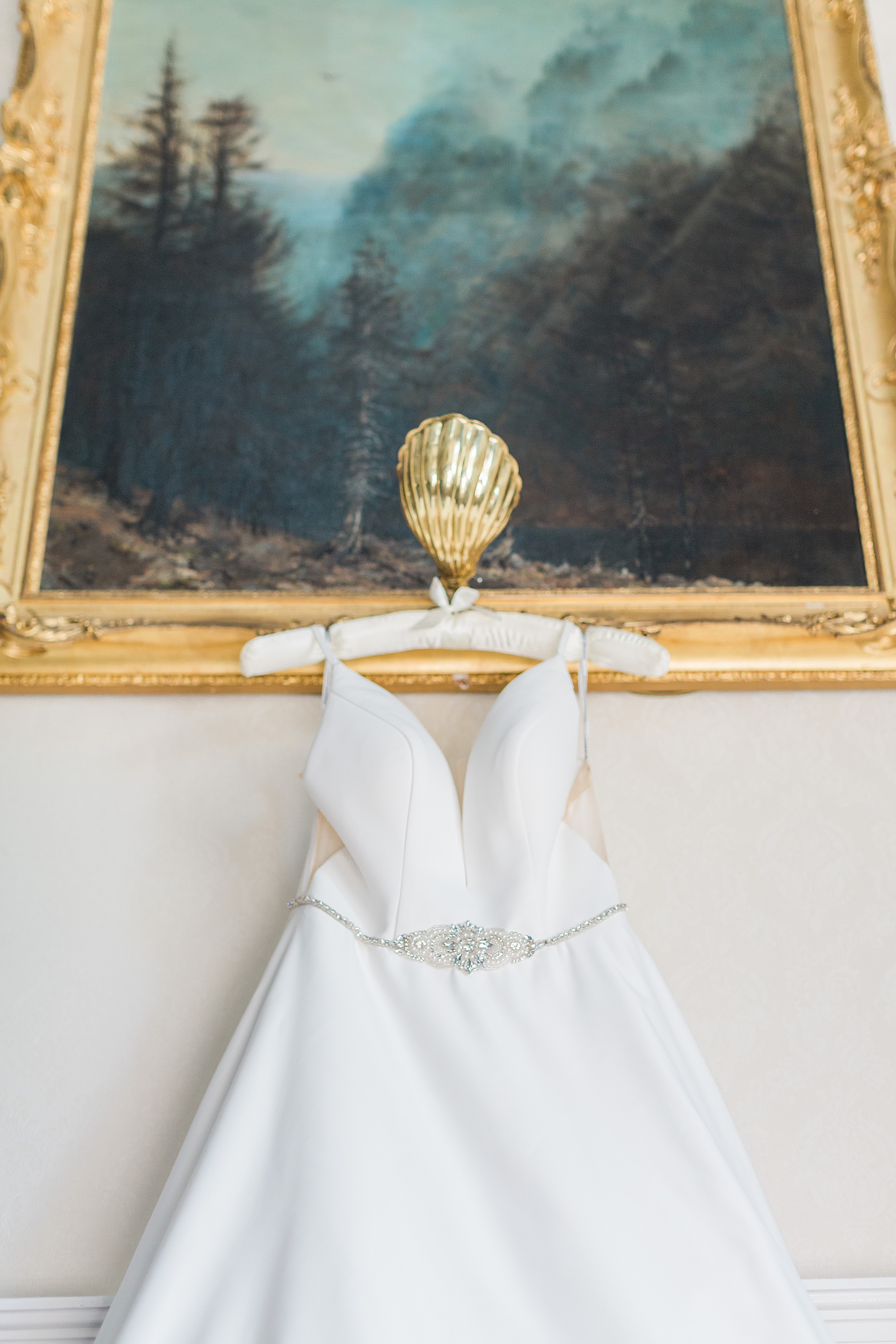 photo of a wedding dress hung from a gold frame against a wall at grafton manor bromsgrove, the dress has jewel detail to a belt 