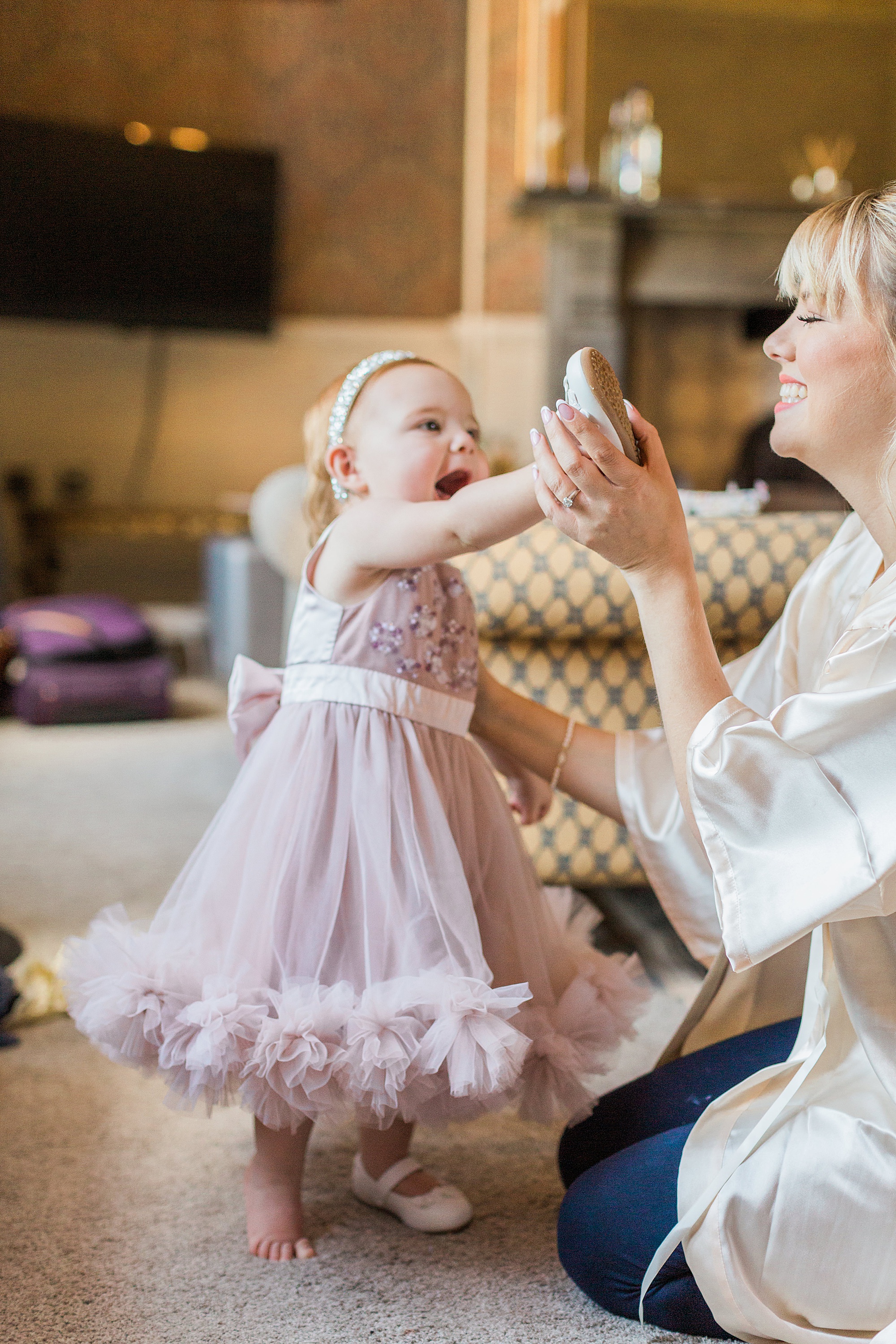 Photo of a bride helping her toddler daughter get dressed with smiles between them
