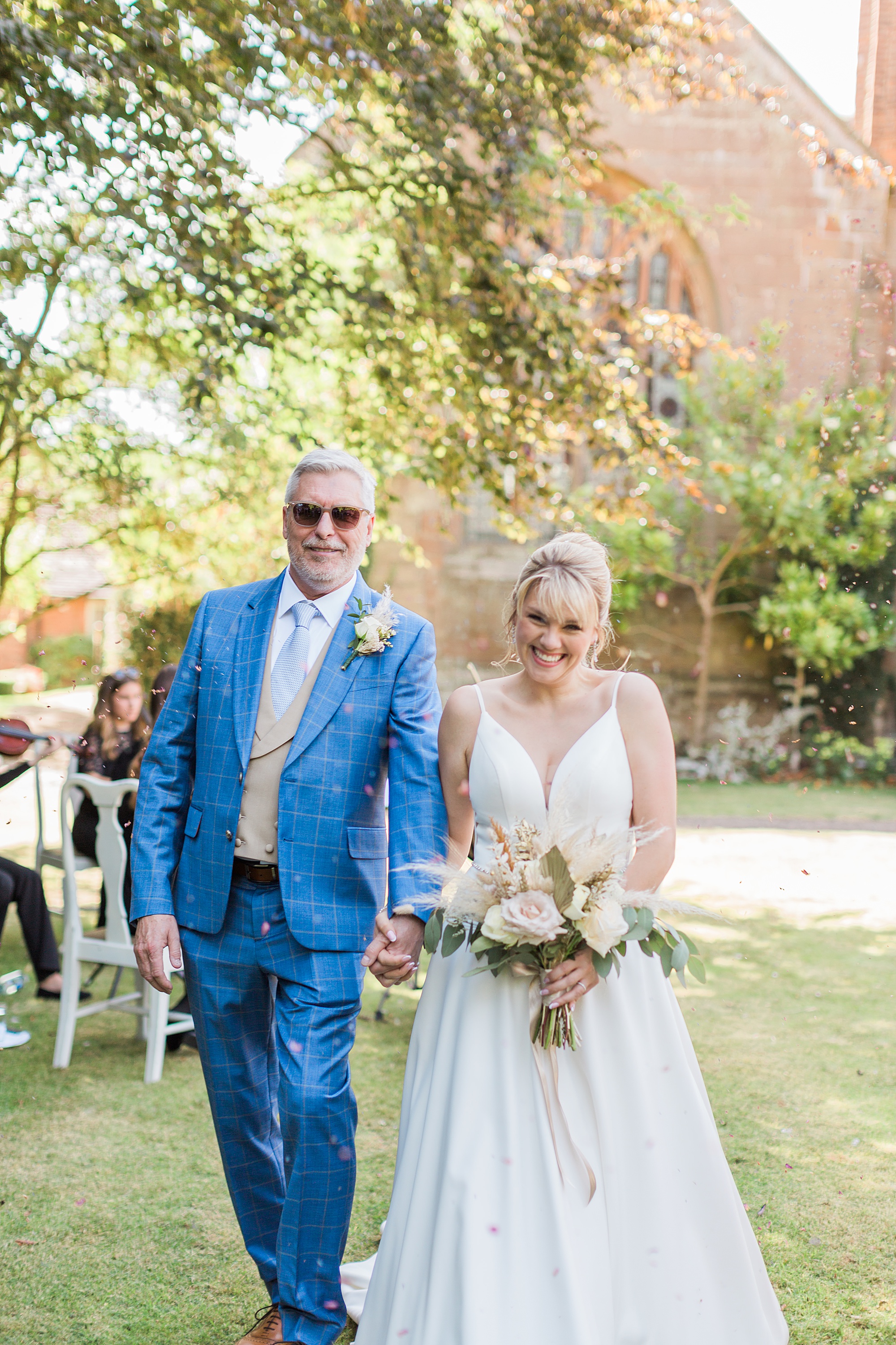 photo shows a bride and groom smiling and laughing as they walk beneath a blanket of confetti being thrown over them 