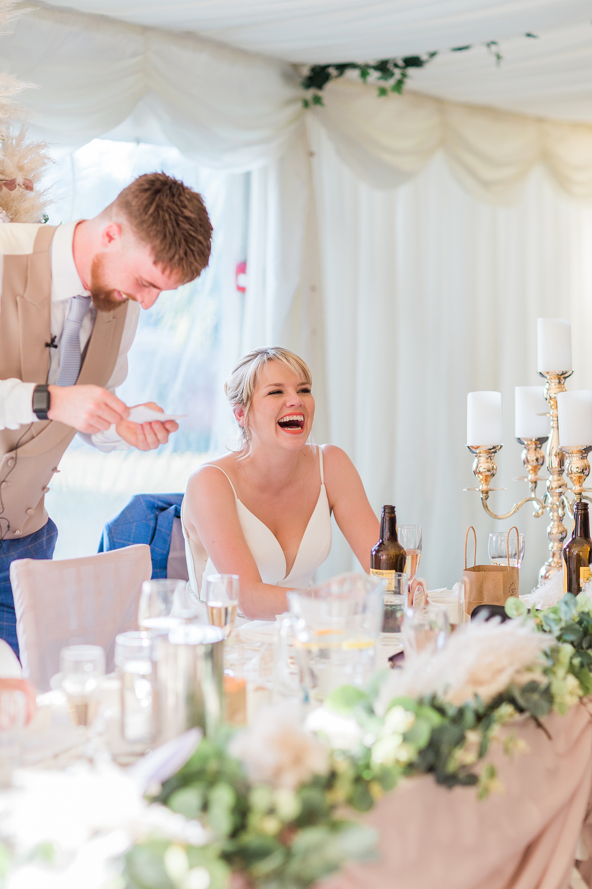 Photo shows a best man speaking at a wedding during the speeches and the bride's reaction next to him 