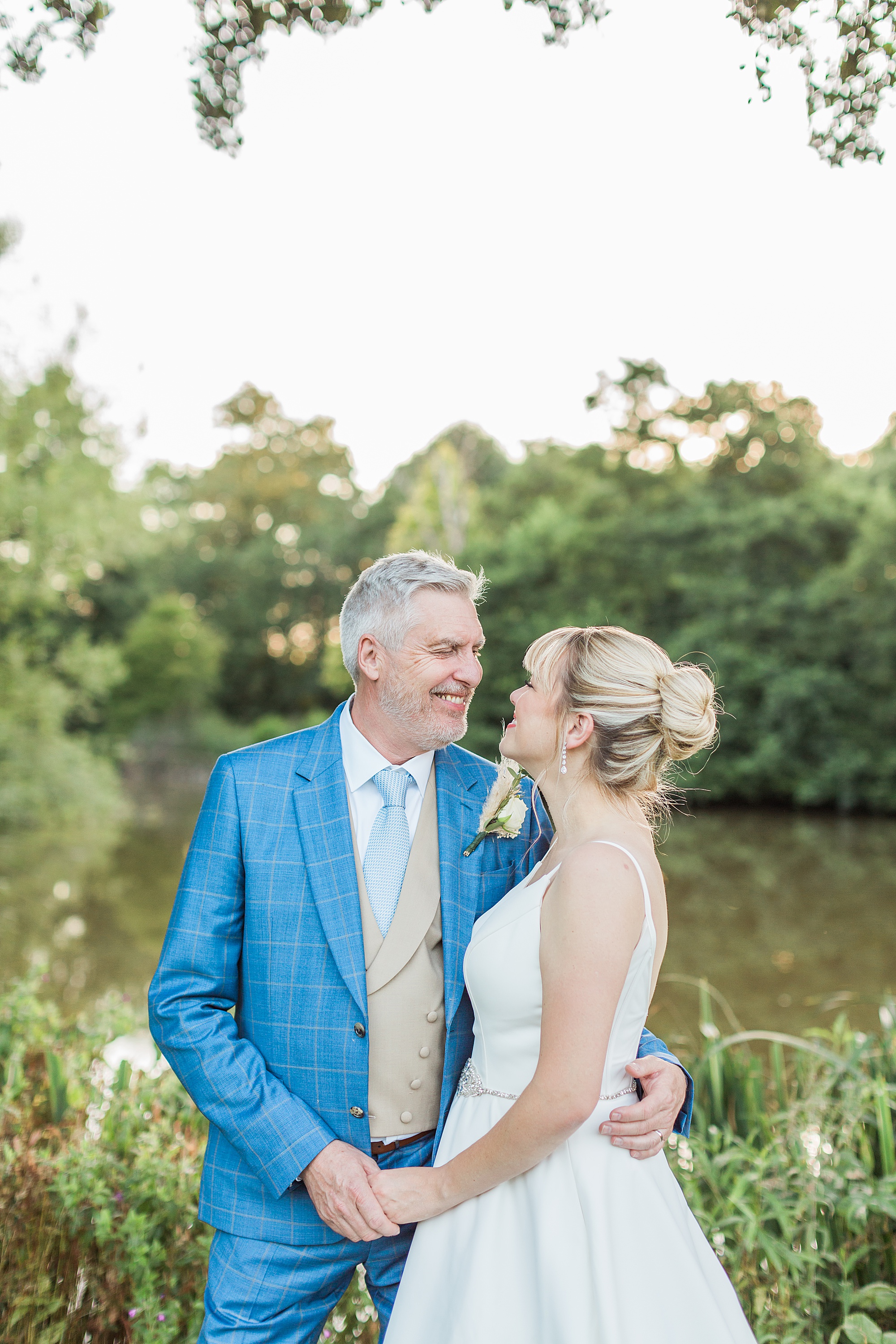 couple posed in front of the lake at grafton manor, they're facing towards each other and holding hands, smiling