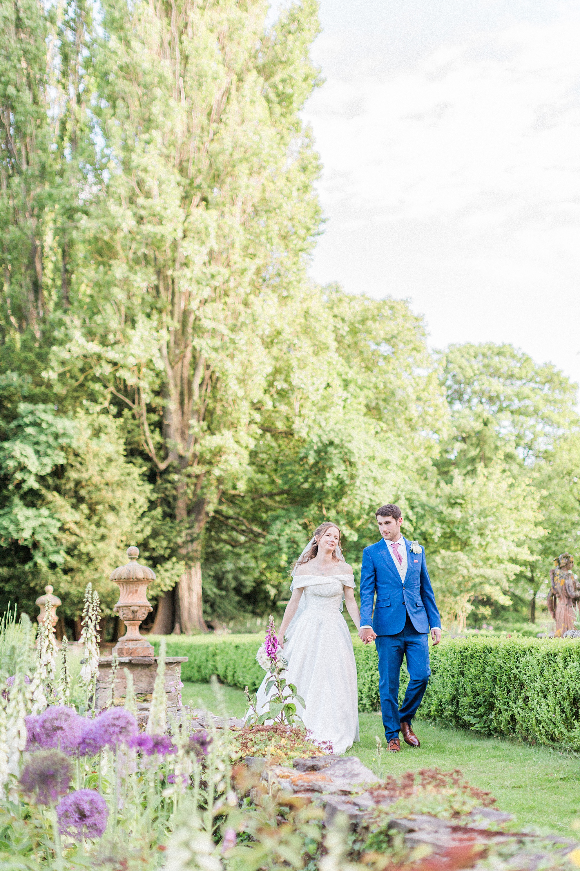 photo of a bride and groom holding hands and walking through a beautifully planted and maintained garden at Hellens Manor in herefordshire