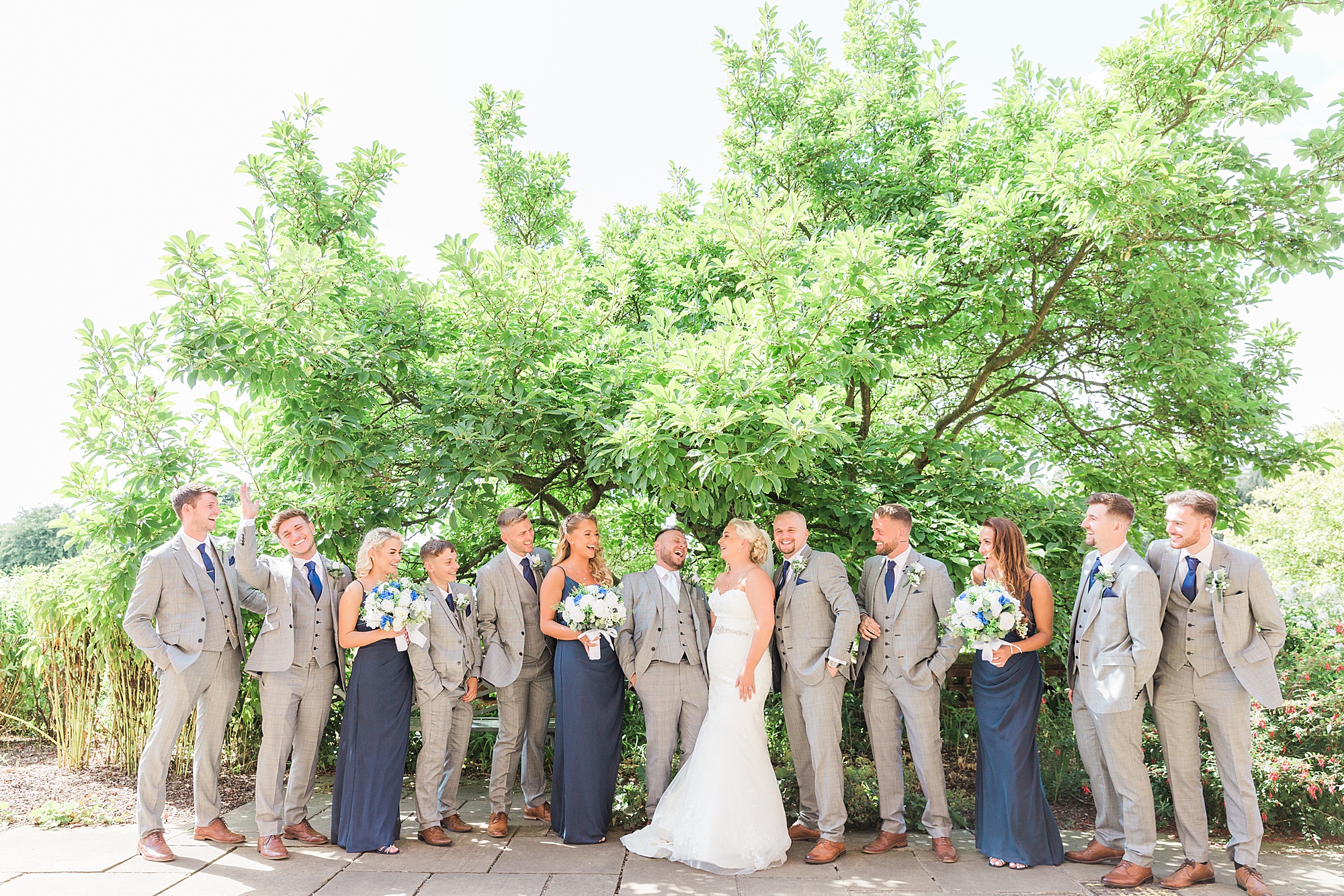 photo of a bride and groom surrounded by their large bridal party each laughing or looking in towards each other smiling posed for a relaxed formal photo 