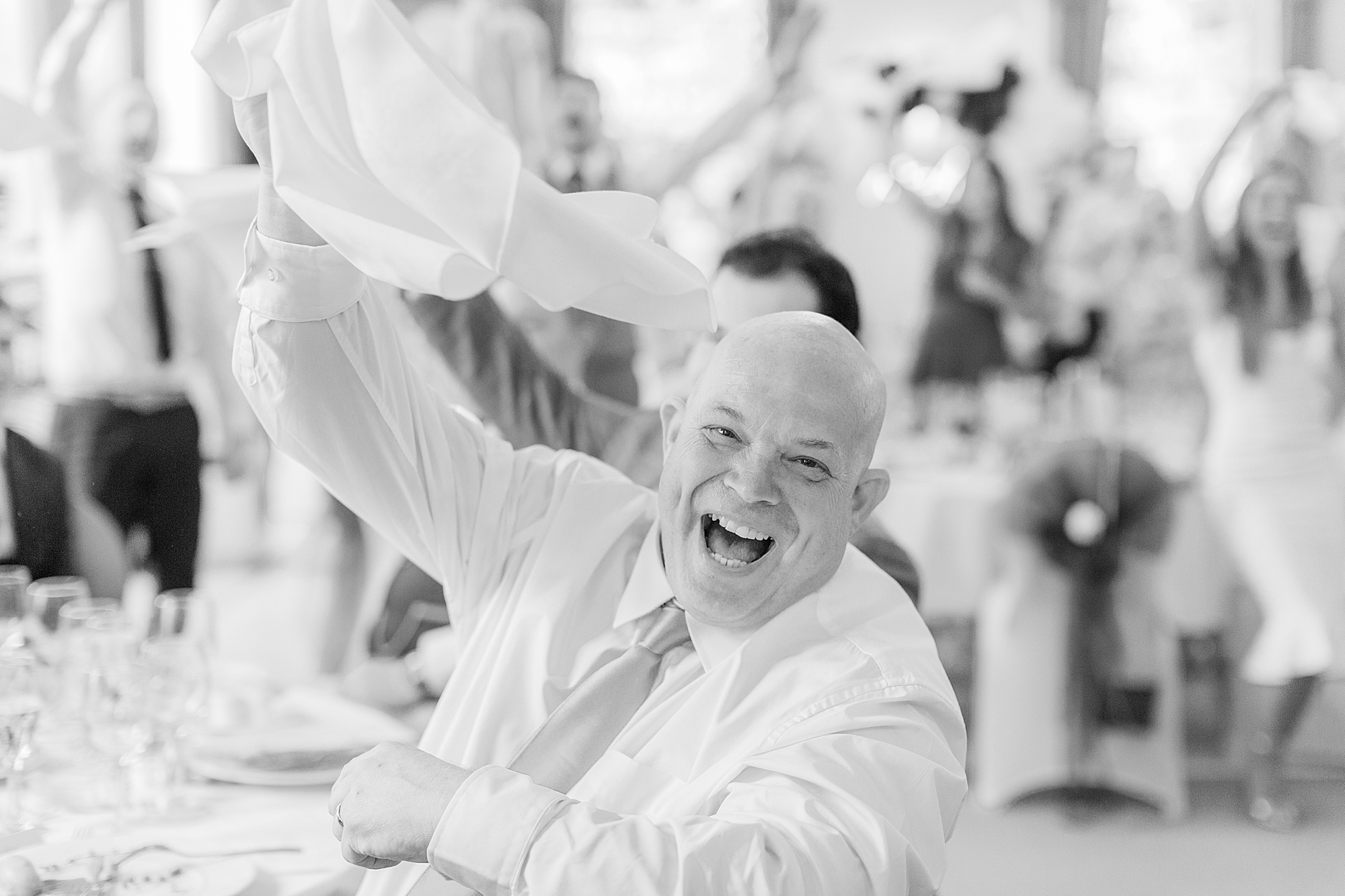 Photo shows a wedding guest holding their napkin in the air and cheering/singing to singing waiters performing
