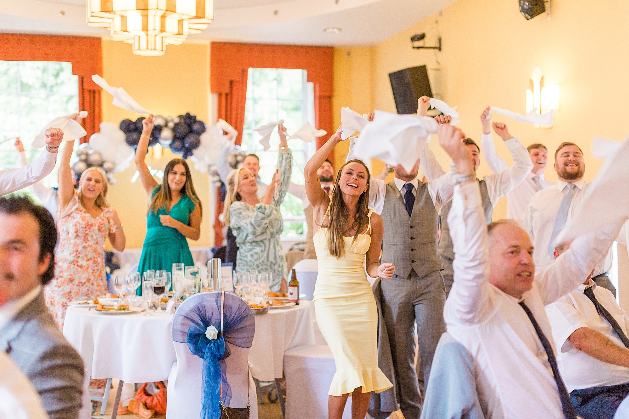wedding guests holding their napkins stood singing and dancing to singing waiters at a wedding reception - image shows so much fun and enjoyment