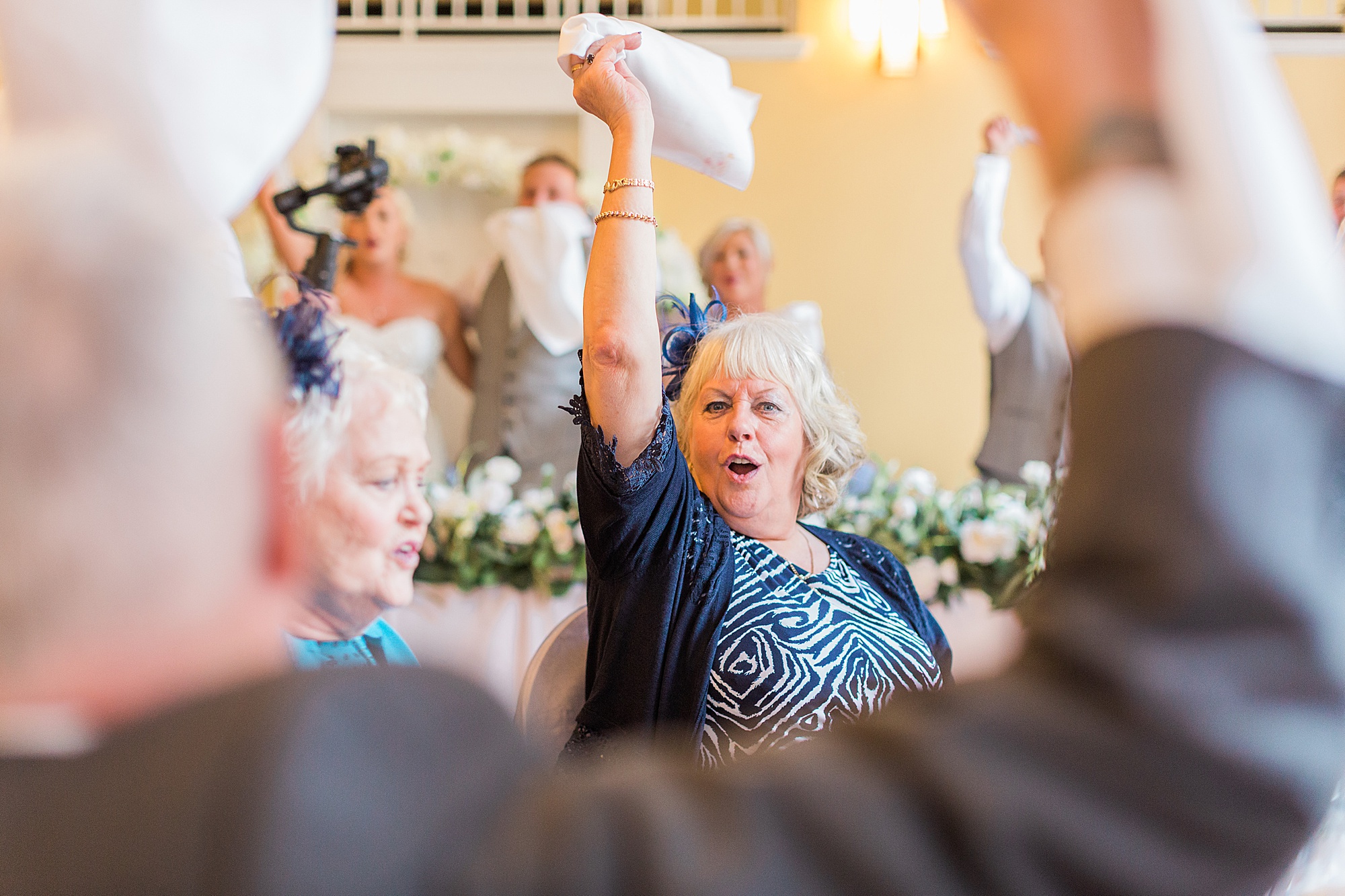 wedding guest swinging her napkin in the airs cheering and singing/dancing to singing waiters at a wedding reception - image shows so much fun and enjoyment