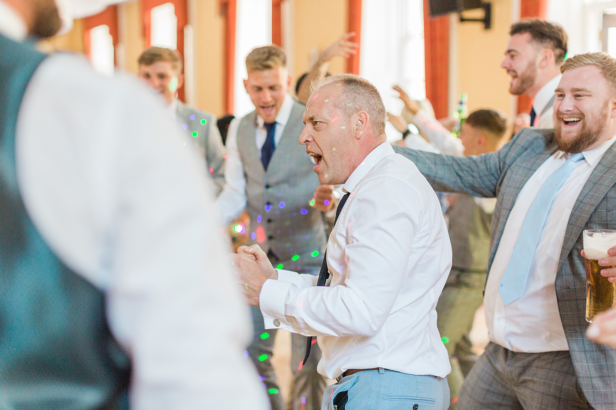 image shows guests dancing and singing at a wedding reception in the evening, they're cheering, mouths open singing, enjoying themselves