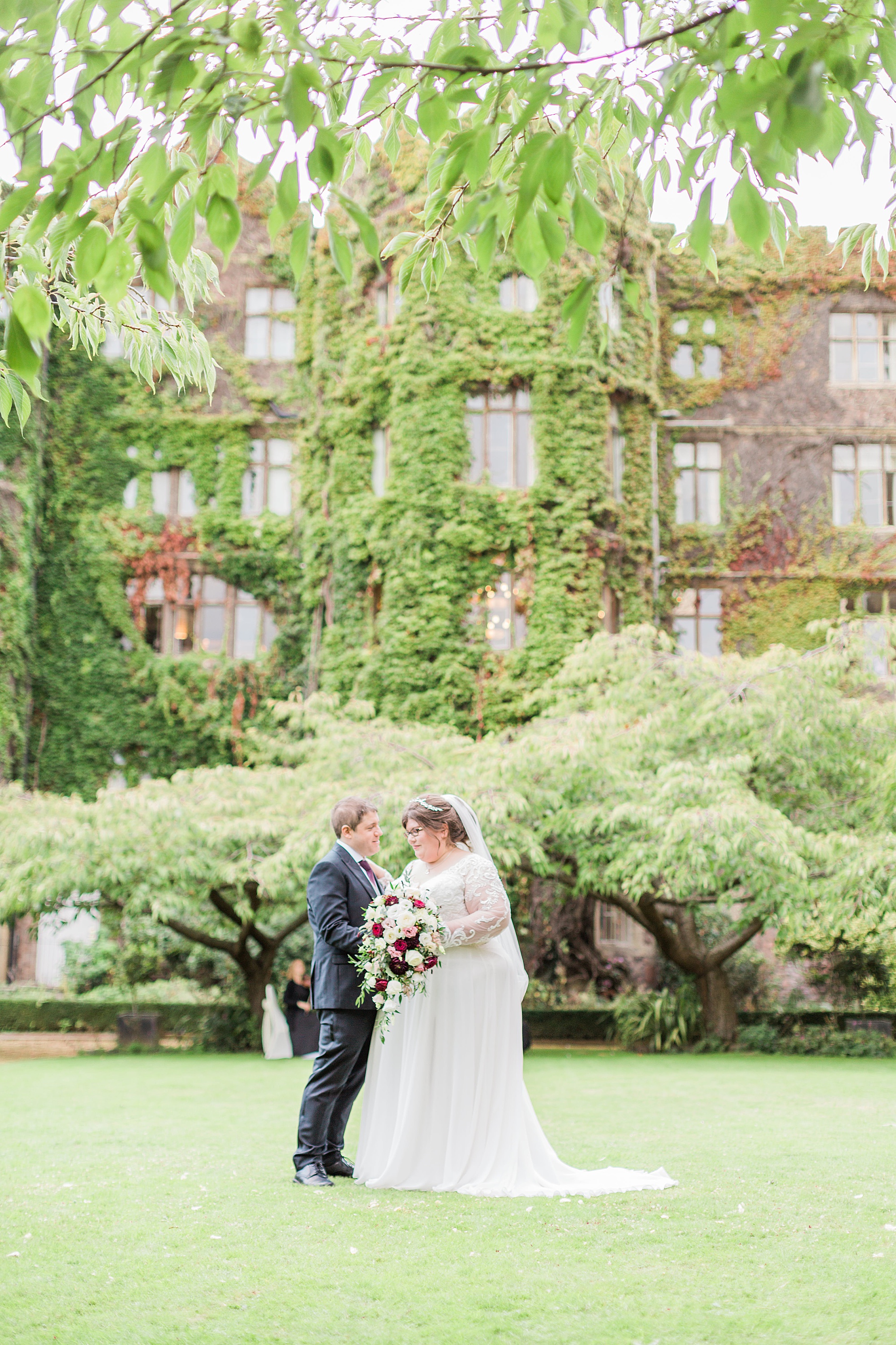 photo of a bride and groom in the grounds of the abbey hotel in malvern, with the abbey hotel behind them, the couple are stood together with trees also behind them