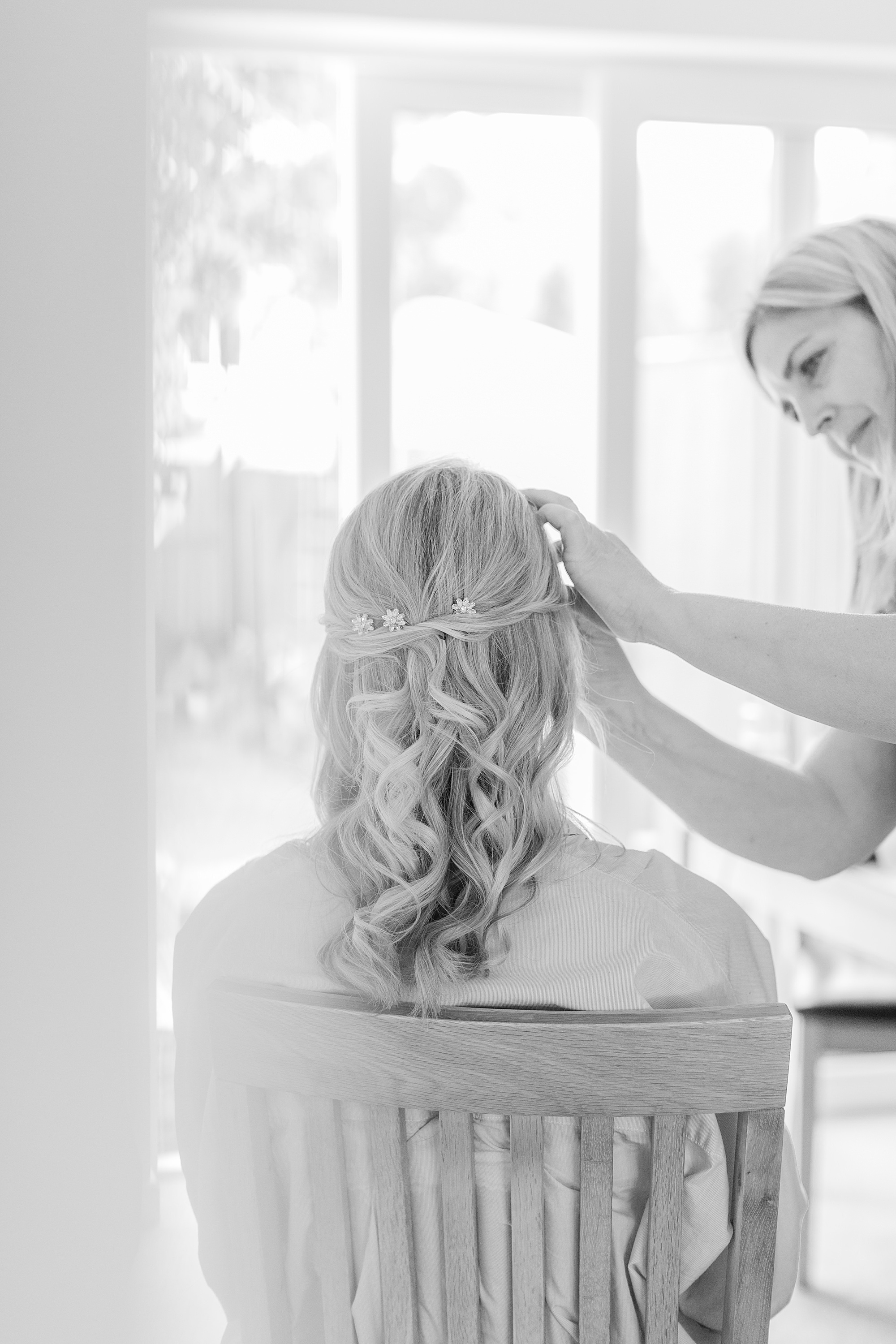 Photo shows a bride having her makeup done on the morning of her wedding. the bride is sat on a chair facing away form the camera