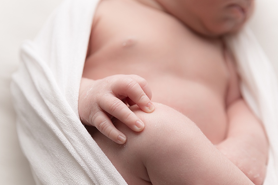Photo by hayley morris Photography trained newborn photographer in malvern worcester. Image shows a newborn baby on white fabric and a white wrap around her, the focus of this image is of her hand and fingers 