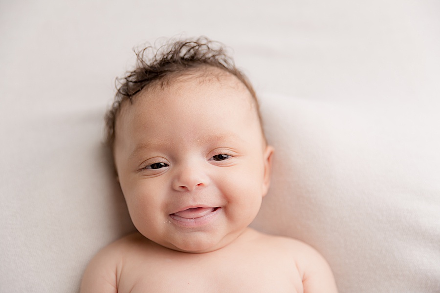 Photo by hayley morris Photography trained newborn photographer in malvern worcester. Image shows a slightly older newborn baby with her eyes open  and smiling lay on white fabric. The image shows from her chest upwards