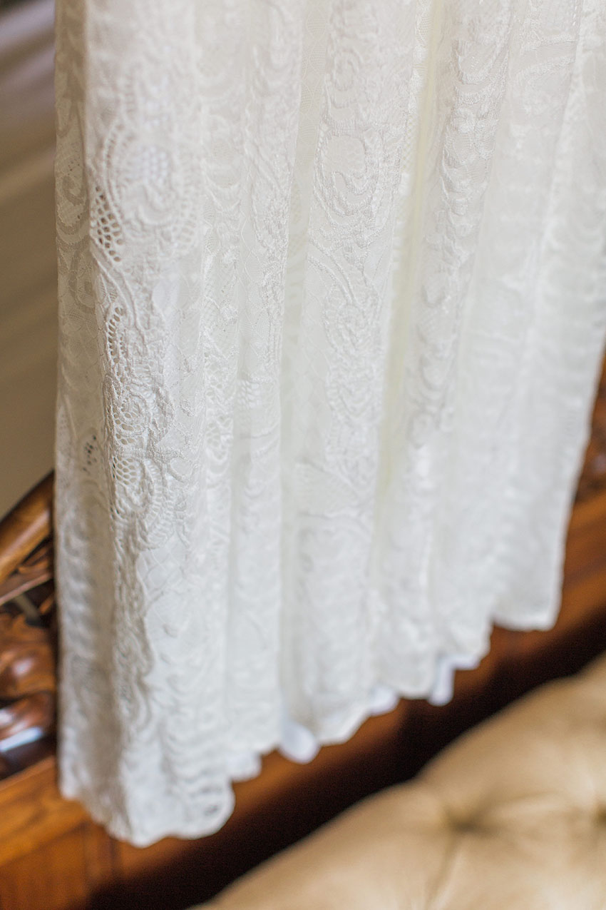 Portrait image of lace bridal dress detail hanging from a four poster bed in the bridal suite of homme house