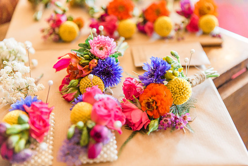 colourful buttonholes and corsages arranged on card ready for guests to place on their suits/wrists