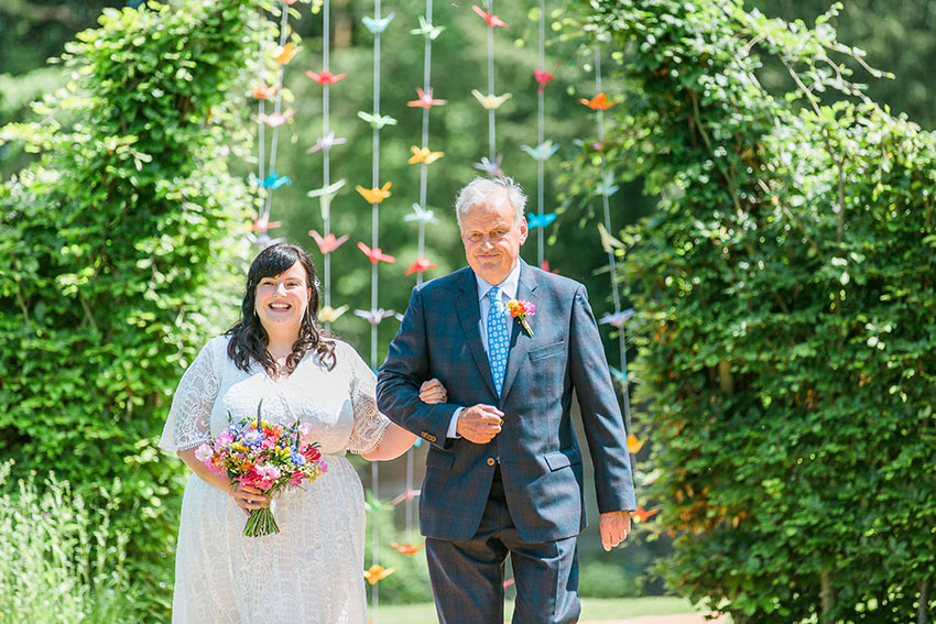 bride and her father walking outdoors in front of origami cranes to the wedding ceremony