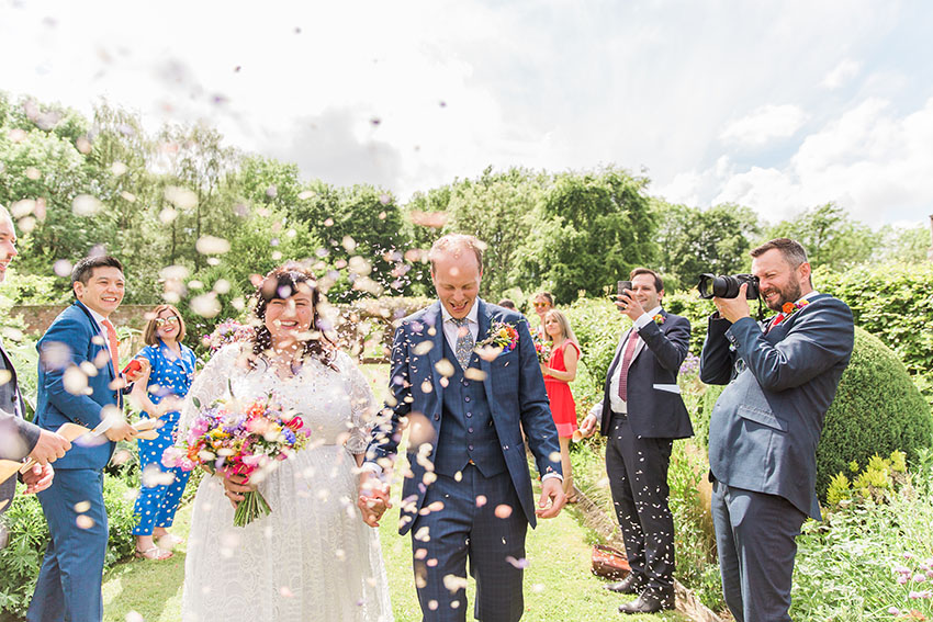 bride and groom outdoors walking through a cloud of confetti being thrown by their weddings guests