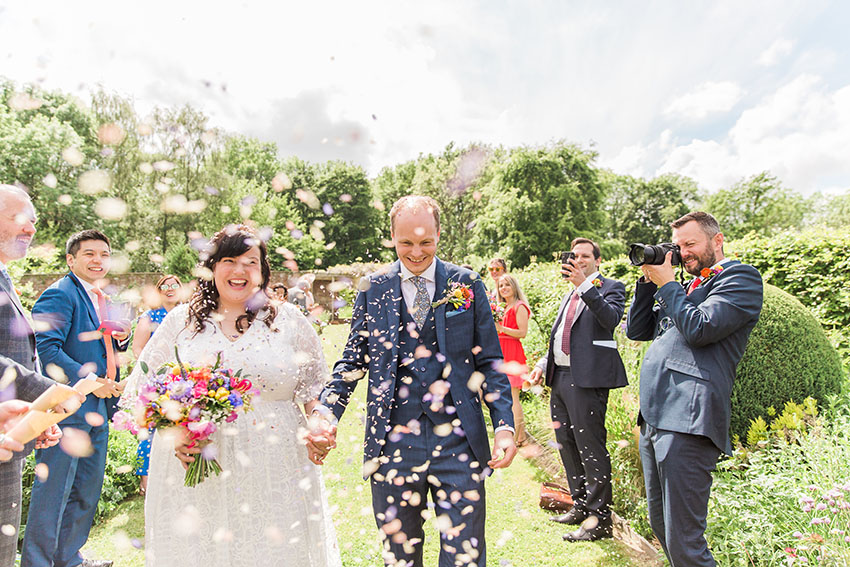 wedding outdoors, bride and groom walking through lots of confetti being thrown over them at homme house in herefordshire