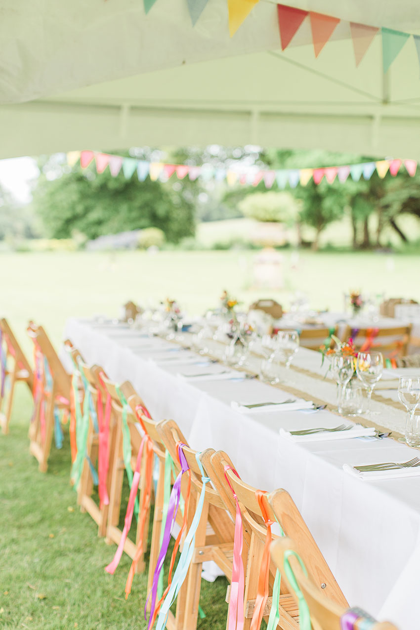 photo of the chairs at an outdoor wedding reception with ribbons handing from the backs, place settings