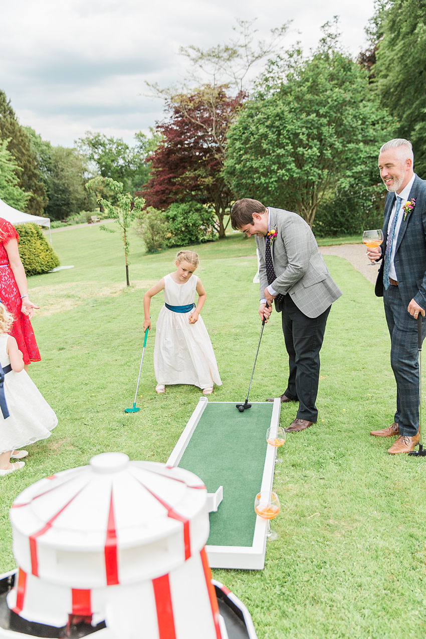 wedding guests and flower girl playing crazy golf on the lawn at a wedding reception