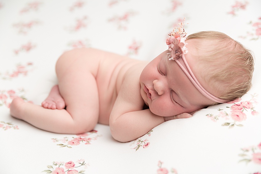 photo of a newborn baby girl posed on her tummy lying on floral fabric. she's wearing a dainty floral headband 