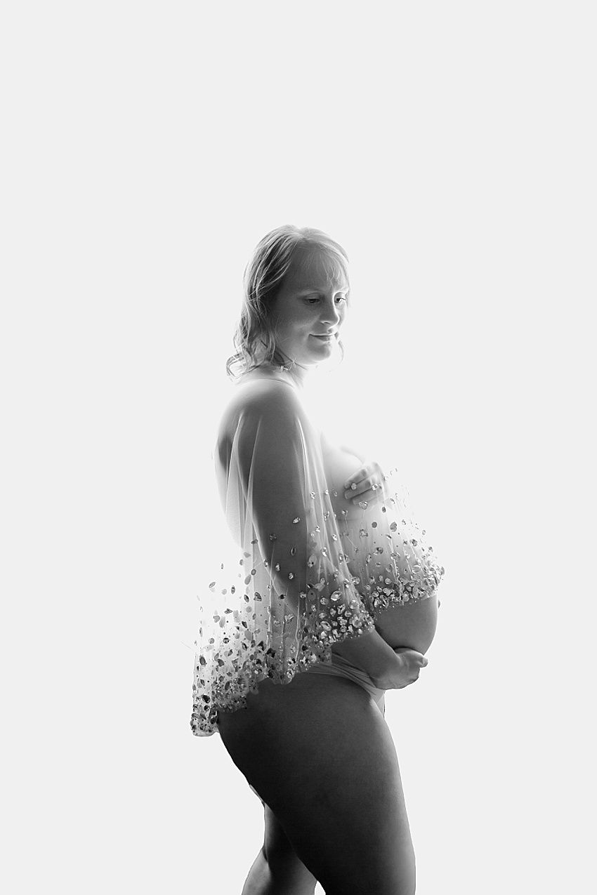 pregnant lady wearing sheer jewelled cape photographed against a white backdrop to form a silhouette with her pregnant tummy