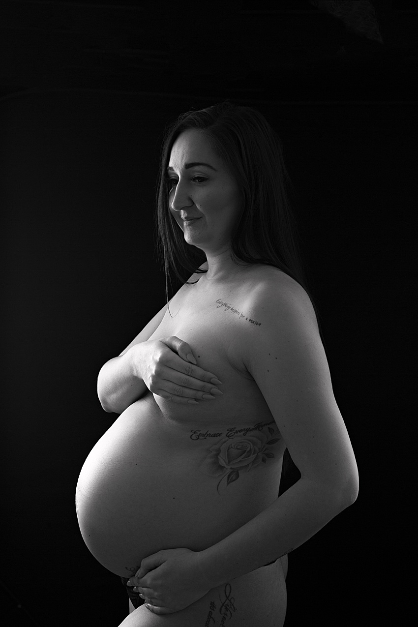black and white photo of a pregnant lady sensitively posed nude holding her chest and pregnant tummy 